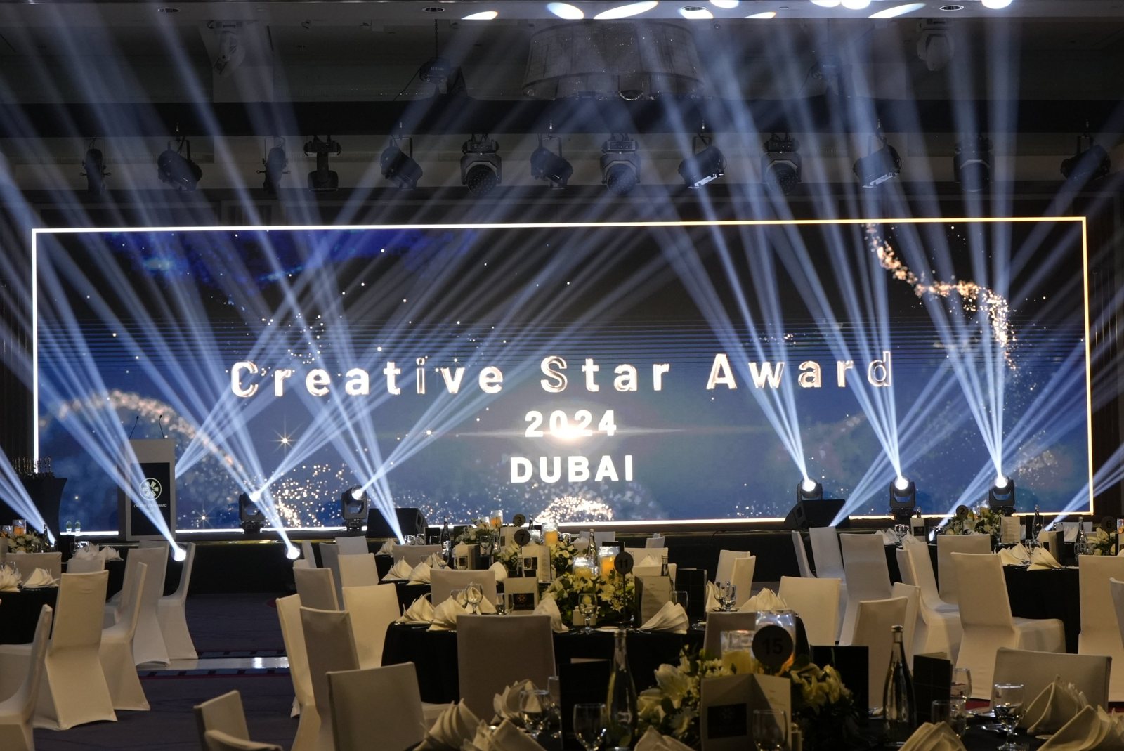 شاشة المسرح تعرض Creative Star Award 2024 دبي فوق طاولات العشاء وأشعة الإضاءة المتقاطعة