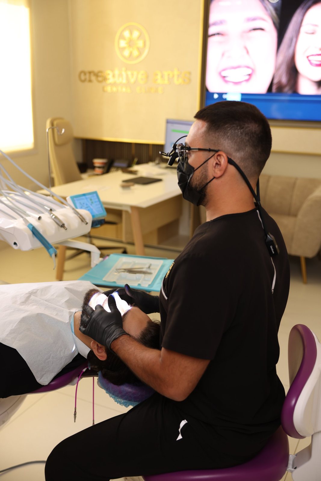 Dentist with loupes treating a bearded patient under the Creative Arts Dental Clinic sign, Dubai